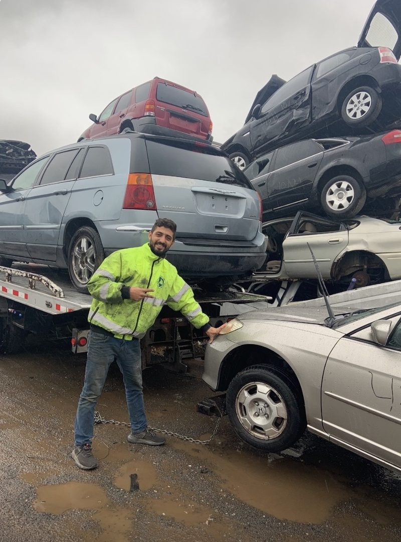 Halsted Cash For Junk Cars tow driver in a hi-vis jacket beside a flatbed stacked with junk cars at the Chicago yard