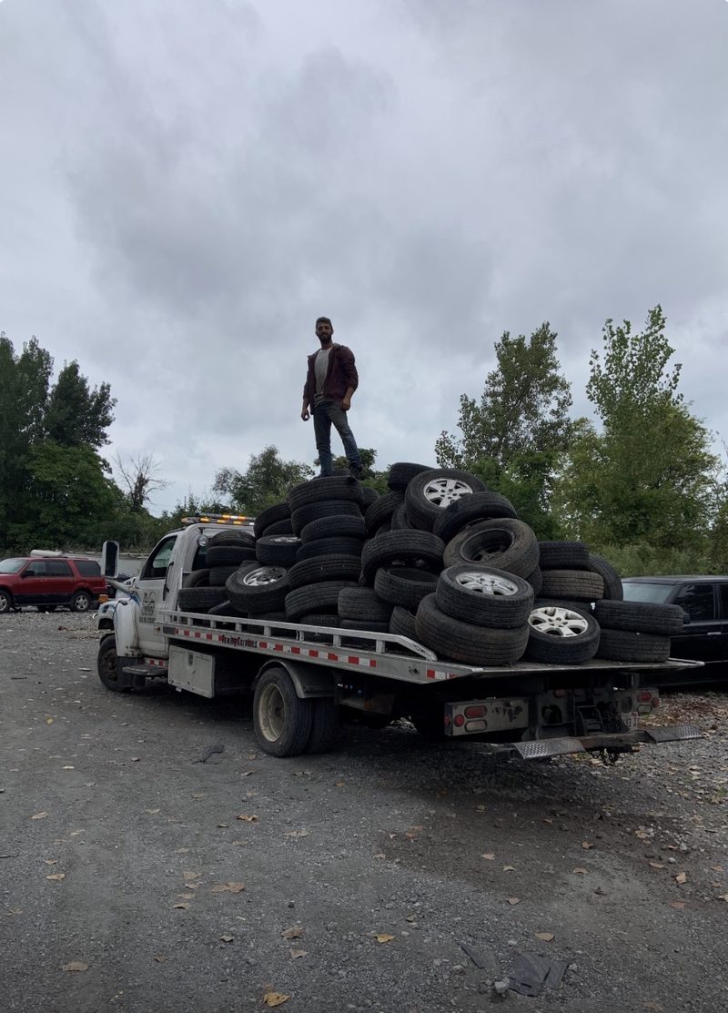 Flatbed tow truck loaded with a pile of scrap tires and alloy wheels pulled from junk cars in Chicago